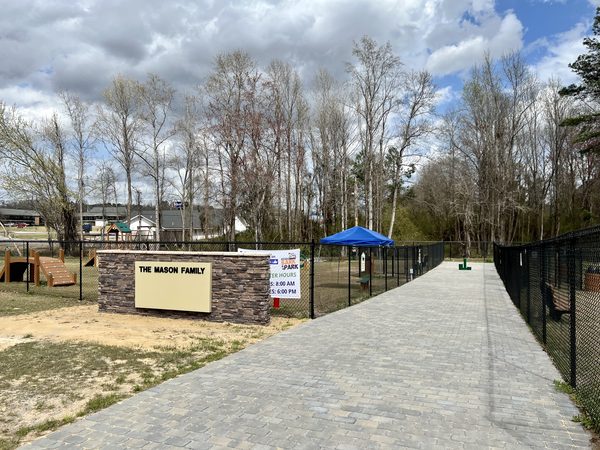 A stone sign reading The Mason Family beside the paved walkway and fenced play areas at the Mason Family Bark Park