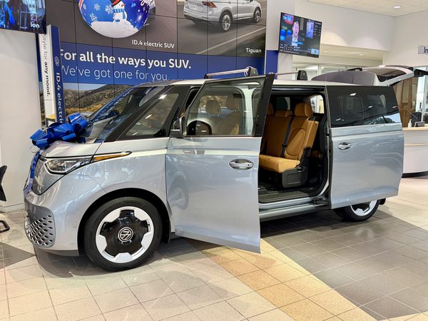 The new silver Volkswagen ID. Buzz with a blue bow and its doors open in a Volkswagen showroom