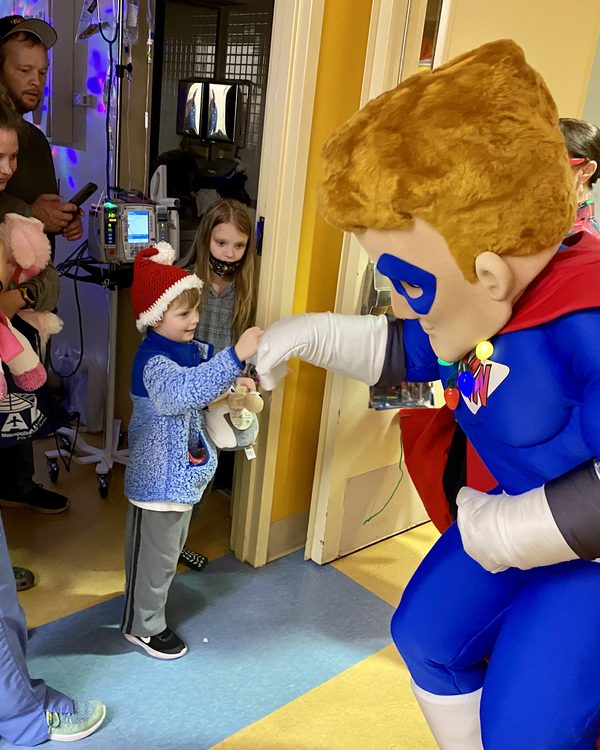 Mighty Max shares a fist bump with a young patient in a Santa hat at the Children's Hospital in Columbia, SC