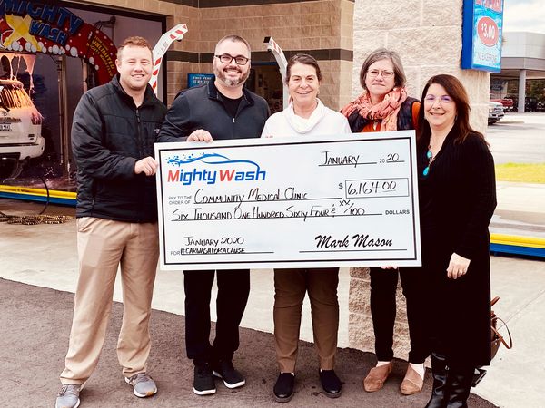 Five people holding a $6,164 Mighty Wash check for the Community Medical Clinic at the car wash