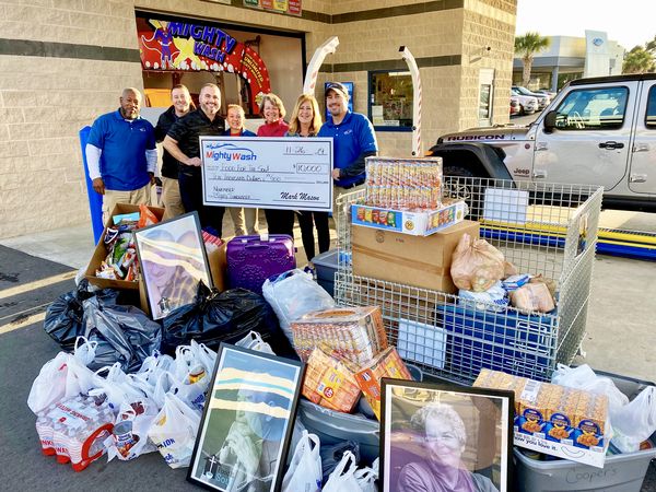Mighty Wash team presenting a $10,000 check to Food For The Soul beside carts and bags full of donated food