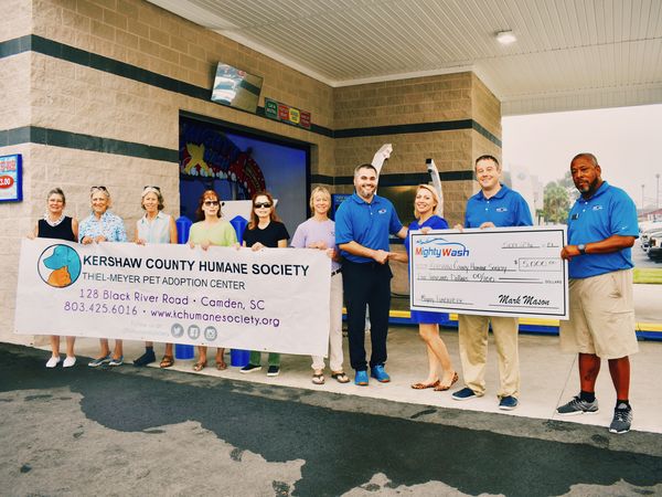 Mighty Wash team members and Kershaw County Humane Society staff holding a $5,000 Mighty Wash check and a Humane Society banner outside the car wash