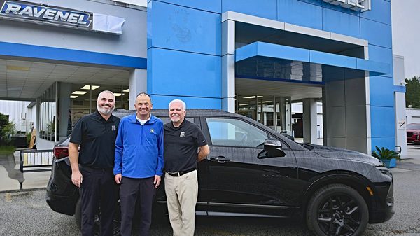 Three men smiling in front of a black Chevrolet Blazer and the Ravenel Chevrolet dealership building