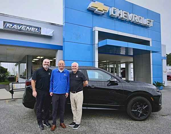 Three men standing in front of a black Chevrolet Blazer at Ravenel Chevrolet, with Chevrolet lettering on the building behind them